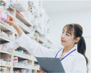 女性の薬剤師が処方せんを見ながら、薬棚から指示された薬を選び出そうとしています