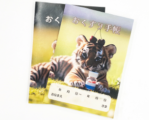 かいけつ薬局のおくすり手帳、表紙は子どものトラが頭にさくらんぼを載せています